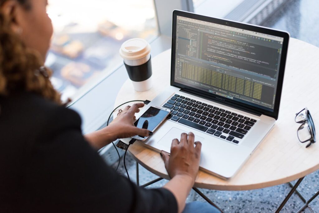 A laptop displaying code alongside a smartphone and a cup of coffee on a table.